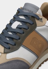 Κοντινό πλάνο ενός μπεζ, γκρι και λευκού αθλητικού παπουτσιού Bogner με μπλε κορδόνια και διάτρητη πλευρική επιφάνεια από τεχνόδερμα σε ταμπά χρώμα.