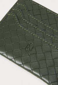 Tarjetero de cuero tejido verde con tres ranuras para tarjetas, costura decorativa y un detalle de logo en relieve.