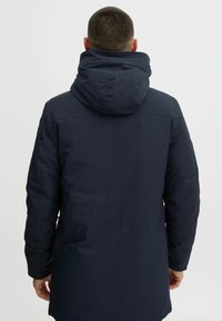 Veste à capuche navy avec une texture lisse, dotée d'un dos légèrement plus long, d'accents cousus et d'une coupe décontractée.