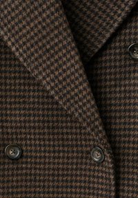 Abrigo cruzado en lana con textura de cuadros en marrón y negro, con grandes botones negros y cuello con solapas.