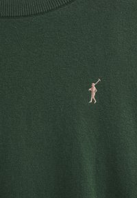 Pull en maille vert avec un col côtelé et une petite figure rose brodée tenant un club de golf sur le côté gauche de la poitrine.