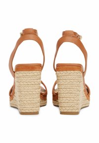 Sandales à talons compensés en cuir marron avec un talon en jute tressé, dotées de brides ajustables à la cheville et de côtés ouverts. Semelle texturée pour une meilleure adhérence.