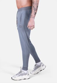 Pantaloni jogger grigi con un design aderente, dotati di tasche laterali, vita con cordoncino e polsini a costine, abbinati a sneakers bianche.
