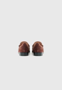Pair of brown suede loafers with low black heels shown from the back on a plain light gray background.