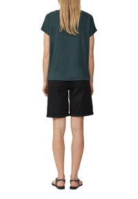 Haut court vert foncé à l'ajustement décontracté, associé à un short en denim noir avec des ourlets roulés et des poches arrière. Porté avec des sandales.