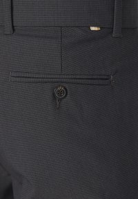  skräddarsydda mörkgrå byxor med en fin rutmönster, som har en bakficka med knapp och subtila sömmar.