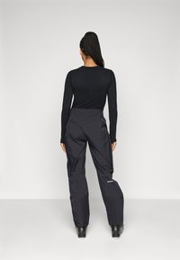 Schwarzes Langarmshirt, kombiniert mit schwarzen, wasserdichten Hosen mit Reißverschlusstaschen und geradem Bein-Design. Eignet sich für Outdoor-Aktivitäten.