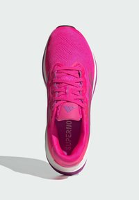 Baskets de sport roses vives avec un dessus texturé, des lacets et un col rembourré. Dispose d'une semelle blanche et violette. Notable branding à l'intérieur.