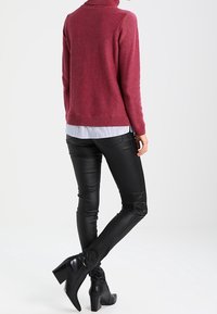 Mjukt vinrött stickat turtlenecktröja med ribbad nederkant, i kombination med figurnära svarta fusklederbyxor och svarta ankelboots.