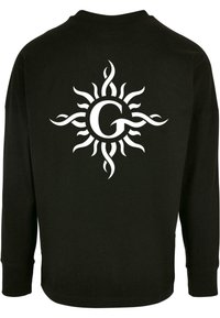 Fekete, hosszú ujjú póló, hátulján fehér napgrafikával, bonyolult kanyarokkal és a középpontban "G" betűvel. Puha szövettextúra.
