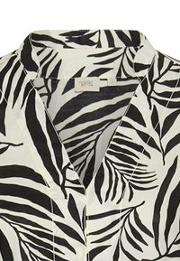 Schwarz-weiße Bluse mit einem Blattmuster, leichtem Stoff, V-Ausschnitt und sichtbaren Nähdetails entlang der Nähte.