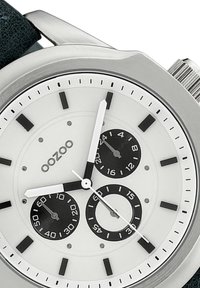 Montre analogique avec un boîtier en acier inoxydable, un cadran blanc, des sous-cadrans noirs et un bracelet en cuir vert. Présente des index noirs et des aiguilles argentées.