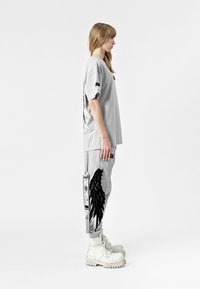 Camiseta oversized gris claro con gráfico de alas negras, combinada con joggers gris a juego que presentan un detalle de alas y botas de combate blancas.