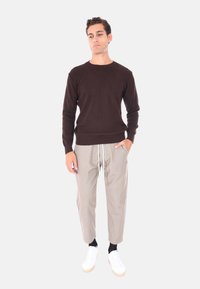 Maglione marrone a costine, pantaloni grigi chiari aderenti con stringhe in vita e sneakers bianche con suole beige. Design semplice, vestibilità casual.
