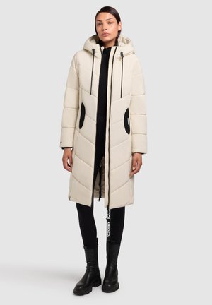 Világos bézs színű, kapucnis pufi kabát, fekete részletekkel és diagonális steppelési mintával. Cipzáras záródás és oldalsó zsebek jellemzik.