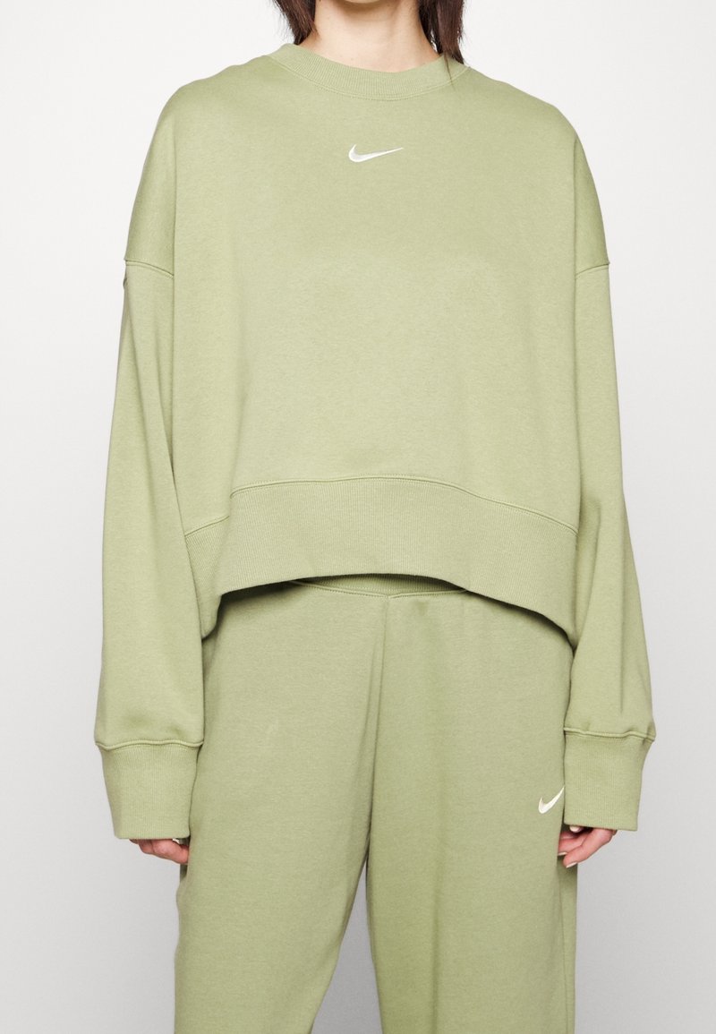 Olivově zelená oversized mikina s kulatým výstřihem a spadlými rameny, s malým bílým logem Nike na hrudi. Hladký materiál.