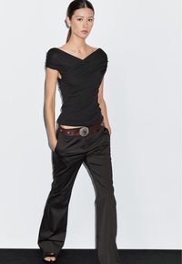 Sort off-shoulder top med draperet design, parret med løse sorte bukser. Brun bælte med en sølv concho accent. Minimalistisk stil.