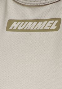 Maglietta sportiva grigia chiara con una trama traspirante, caratterizzata da un logo Hummel bianco prominente su uno sfondo rettangolare verde.