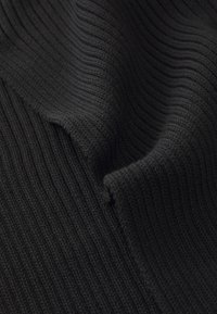 Tissu en tricot noir à côtes avec une texture douce, présentant un drapé ondulé et des lignes verticales régulières et uniformément espacées.