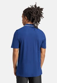 Polo blu con maniche corte e bordo del colletto bianco. Tessuto liscio, vestibilità regolare, vista posteriore che mostra i dettagli delle cuciture.