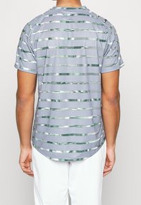 Camisa de manga corta de color gris con un patrón que presenta rayas horizontales en verde y acentos metálicos, hecha de una tela ligera.