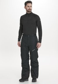 Sort termisk top med halv lynlås krave, parret med sorte isolerede bukser. Bukserne har sidelommer og et logo på underbenet.