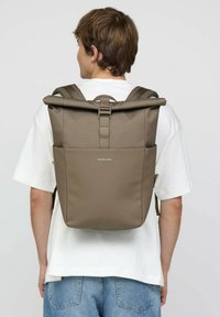 Brauner Roll-Top-Rucksack mit gepolsterten Schulterriemen, Fronttasche und Logo-Detail. Hergestellt aus strapazierfähigem Stoff mit einem schlanken, minimalistischen Design.