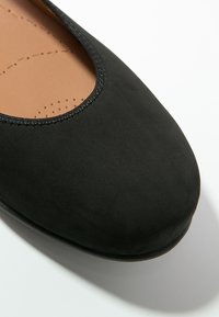 Gros plan sur une ballerine noire en daim avec un bord cousu et une semelle intérieure rembourrée beige perforée.