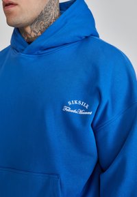 Felpa blu realizzata in tessuto morbido, con una tasca frontale, cappuccio regolabile con cordino e branding in bianco sul petto.