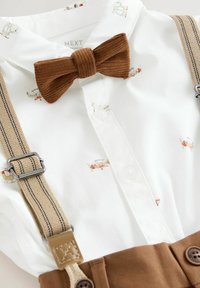 White collared shirt with airplane print, brown corduroy bow tie, and beige suspenders with brown leather accents and stitching details.