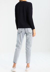 Marineblauwe trui met structuur en lange mouwen, gecombineerd met lichtblauwe jeans met hoge taille; witte sneakers met metallic accenten.