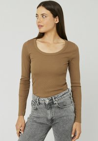 Haut marron à manches longues avec un col rond et une texture côtelée, associé à un jean taille haute gris clair avec une fermeture à bouton.