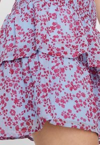 Světle modrá vrstvená sukně s květinovým vzorem v odstínech růžové. Vybavena nařaseným pasem a volánkovým lemem pro zvýšenou texturu.