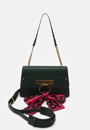 Bolso Love Moschino en verde oscuro con correa de cadena dorada, detalle de anillo dorado y pañuelo negro y rojo atado en un lazo en la parte delantera.