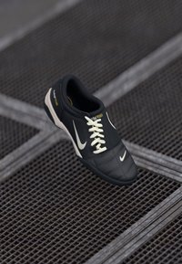 Crno-bijeli Nike tenisice s vezicama, s oznakom "total 90 III", smještene na metalnoj mrežastoj površini.