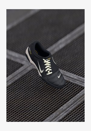 Fekete-fehér Nike sneaker fűzős kivitelben, "total 90 III" felirattal, fémrácsos felületen elhelyezve.