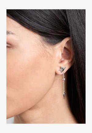 Brincos de prata com um pino em forma de estrela, guias de corrente penduradas e acentos em forma de pico, exibindo um design elegante e moderno.