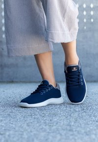 Granatowe sportowe buty dzianinowe z jasnoszarym akcentem na pięcie, białą podeszwą i okrągłym wiązaniem na sznurówki; noszone ze spodniami w paski.