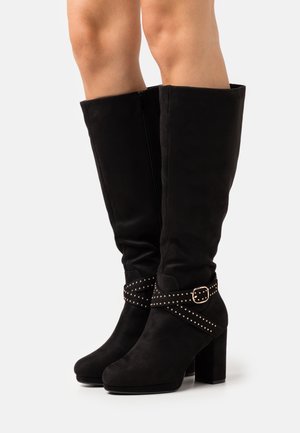 Bottes noires montantes jusqu'au genou en daim, avec une sangle cloutée à boucle, un bout carré et un talon bloc épais. Texture lisse.
