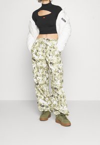 Svart croppad topp med ett utskuret mönster, vit pufferjacka och gröna mönstrade cargobyxor. Gröna sneakers fulländar outfiten.