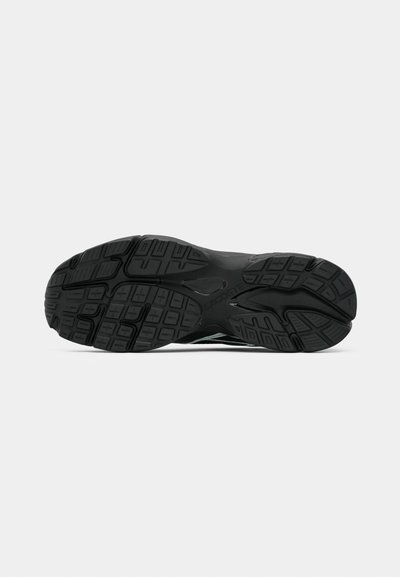 Semelle de chaussure de sport noire avec un motif de bande de roulement texturé, comprenant diverses rainures et crêtes pour l'adhérence et la traction. Le logo "Lacoste" est visible.