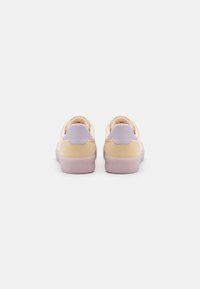 Zapatillas alegres con una parte superior de ante beige y acentos de cuero lavanda, que cuentan con una suave suela de goma lilac y una forma redondeada.