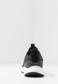 Černé atletické tenisky s texturovaným síťovaným svrškem, polstrovaným límcem, poutkem a kontrastní bílou mezipodešví s mírně zakřiveným tvarem.