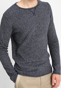 Chemise à manches longues bleu marine en tissu texturé, avec un col rond et des détails cousus au niveau du cou. Coupe ajustée.