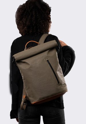 Roll-top backpack in olive green, made of textured waterproof material. Features a front zip pocket and a brown leather base. Adjustable straps.
