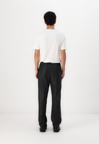 Camiseta blanca de manga corta combinada con pantalones negros de rayas finas y corte holgado. Los pantalones cuentan con una cintura elástica y dos bolsillos traseros.