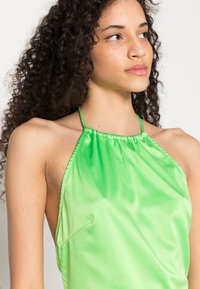 Top halter verde feito de tecido brilhante, com decote franzido e design simples, com alças finas e caimento descontraído.