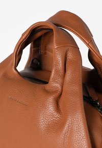 Bruine leren handtas met een gestructureerd ontwerp, een textuurafwerking en onderscheidende handvatten, met een ritssluiting en logo detail.