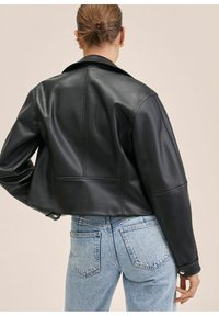 Sort læder cropped jakke med krave og synlige sømdetaljer, parret med lyseblå høj talje jeans. Glat tekstur i hele jakken.