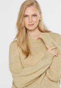 Helles beiges Strickpullover mit lockerer Passform, gerippten Bündchen und einer strukturierten, weichen Optik. Das Material wirkt gemütlich und entspannt.